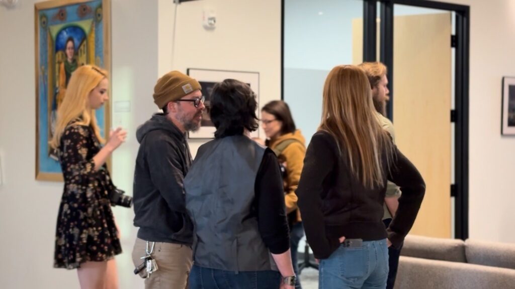 A group of people gather to view art works at 79West show.