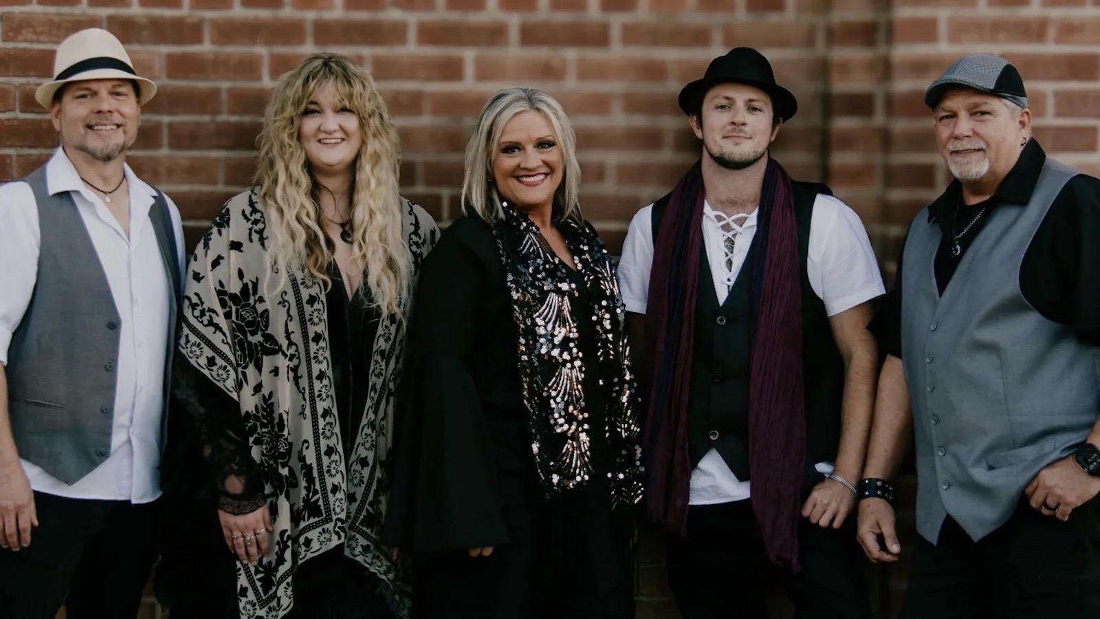 Members from the band The Chain pose in front of a brick wall.